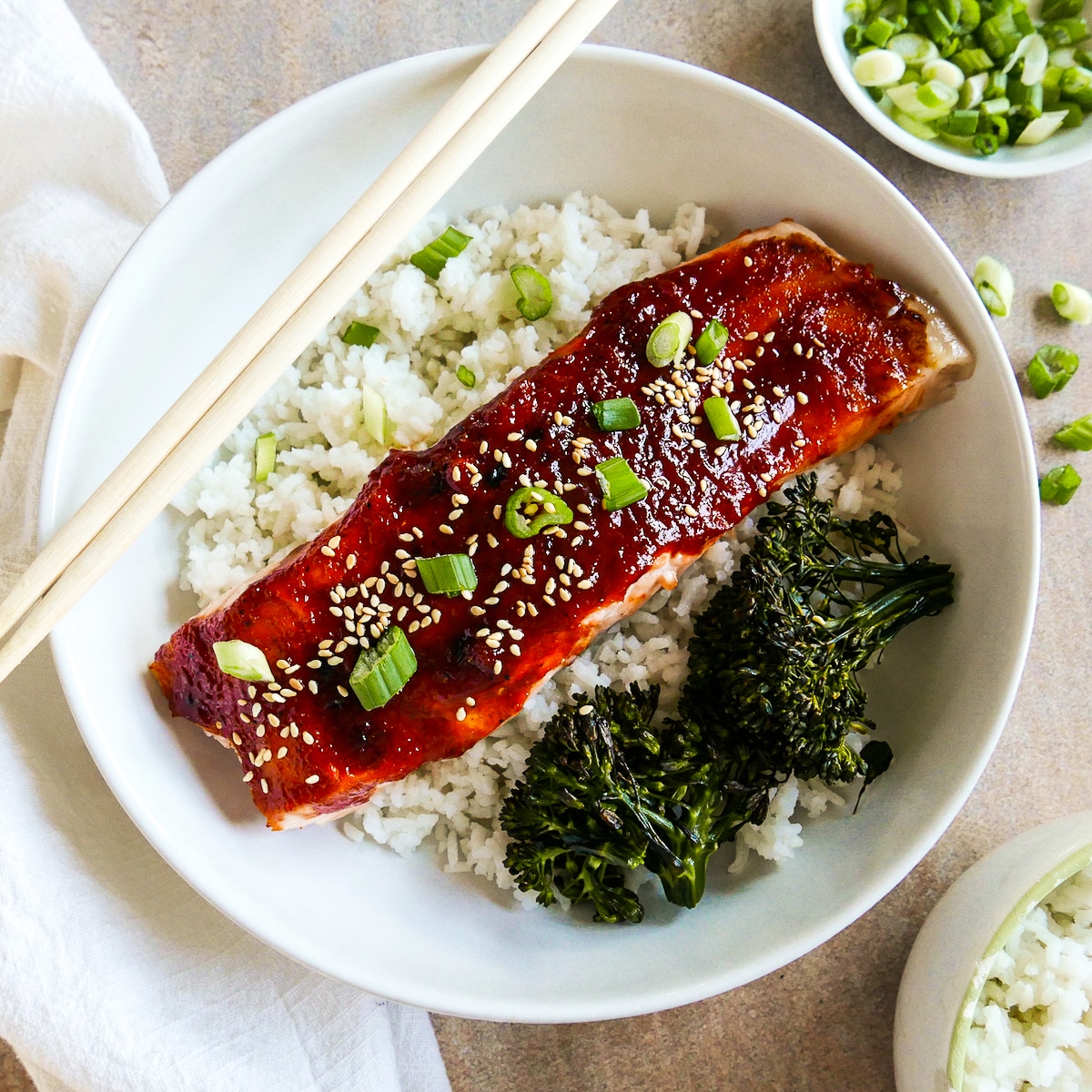 fillet of gochujang glazed salmon on rice in a bowl with chopsticks. 