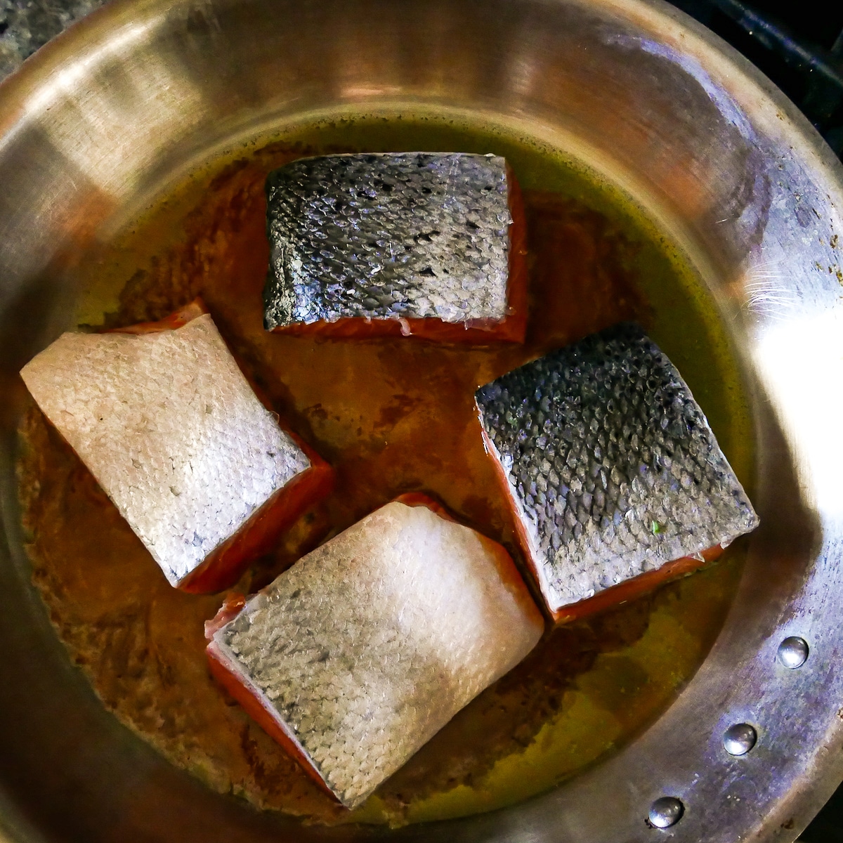 four salmon fillets added to a hot skillet, skin side up.