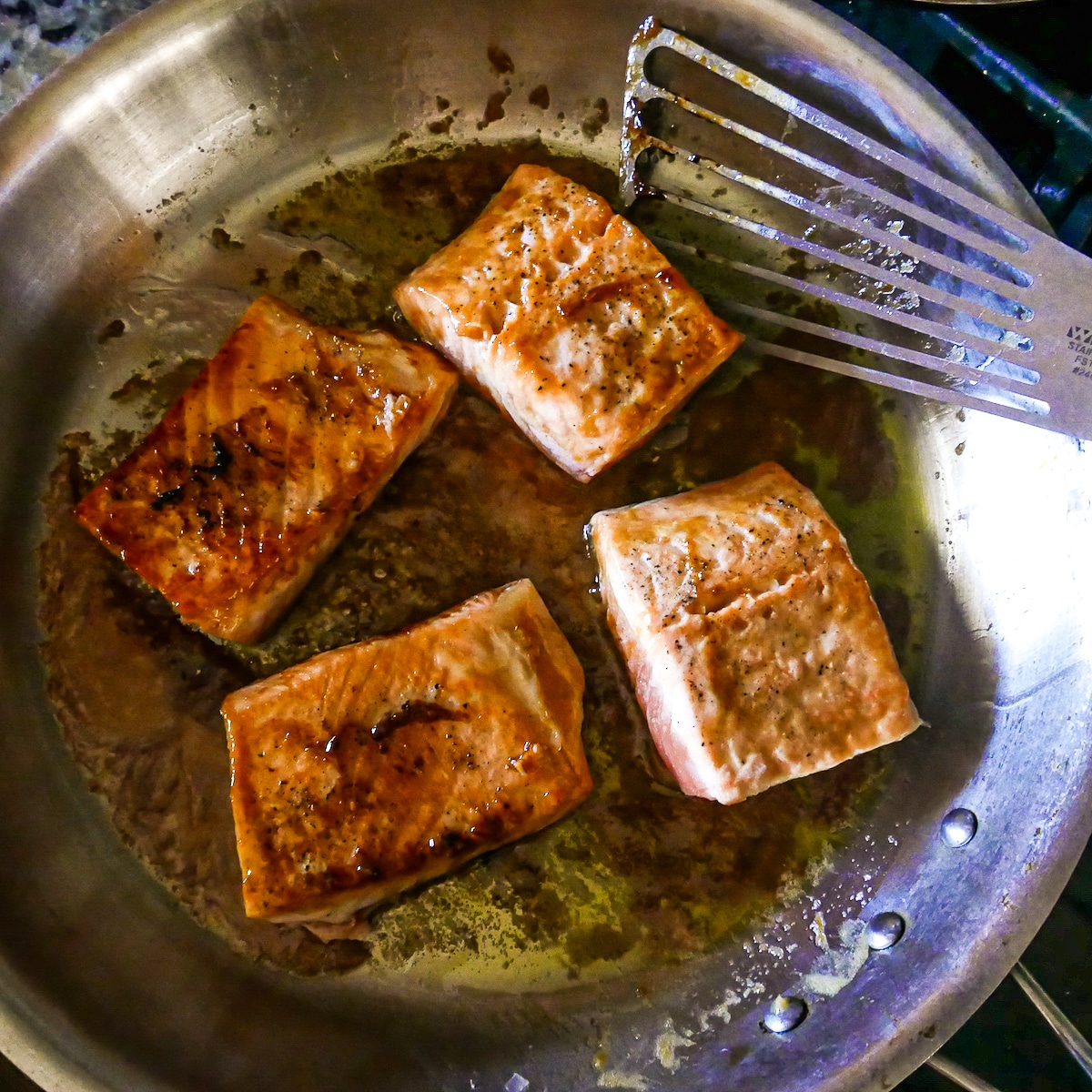 salmon cooking in a large skillet with a fish spatula.