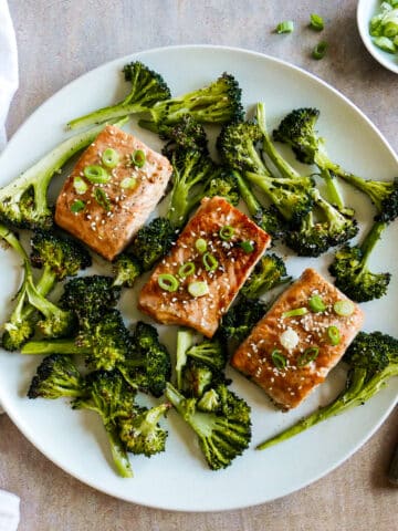 three fillets of miso salmon on a white platter with roasted broccoli.