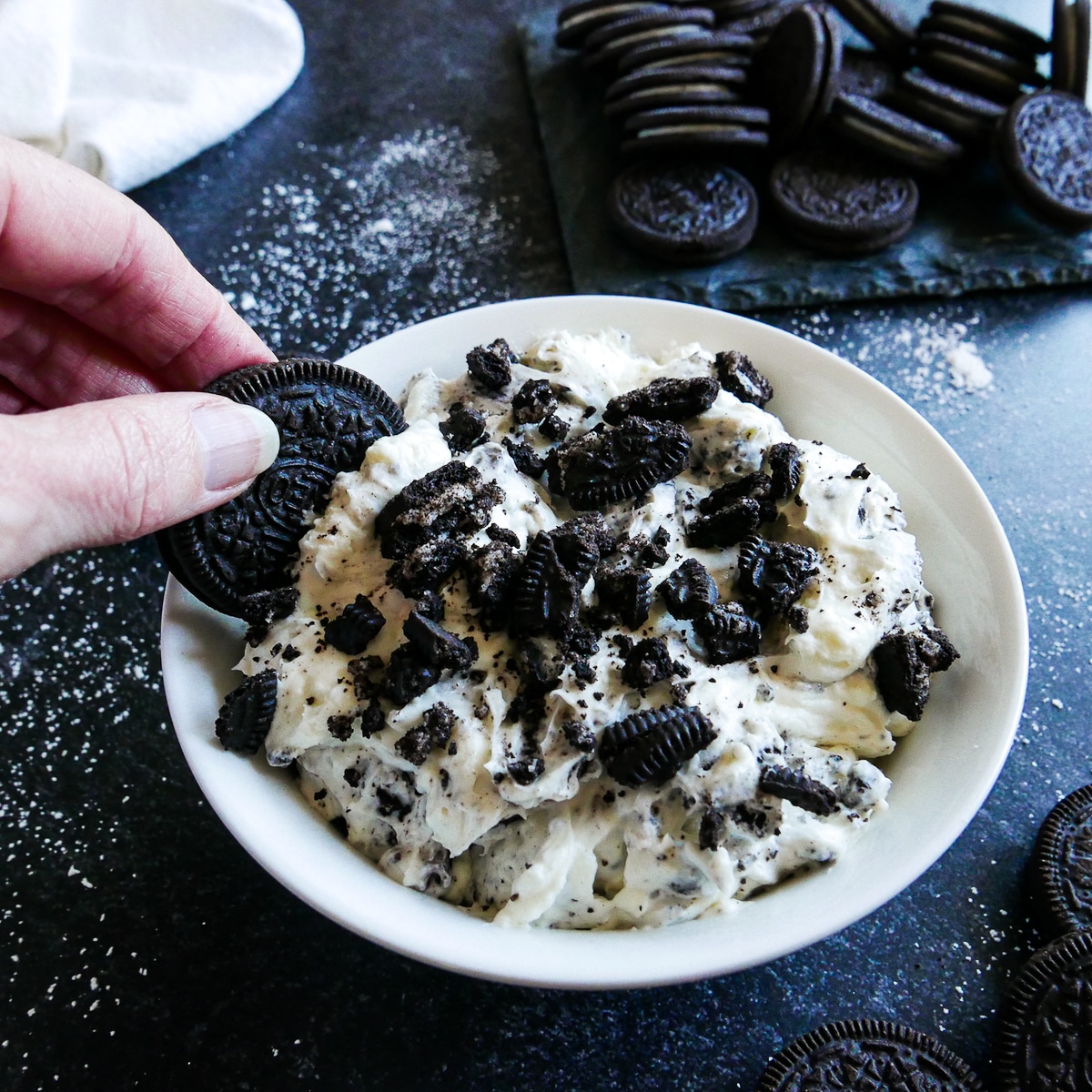 white hand dipping an oreo into oreo cream dip.