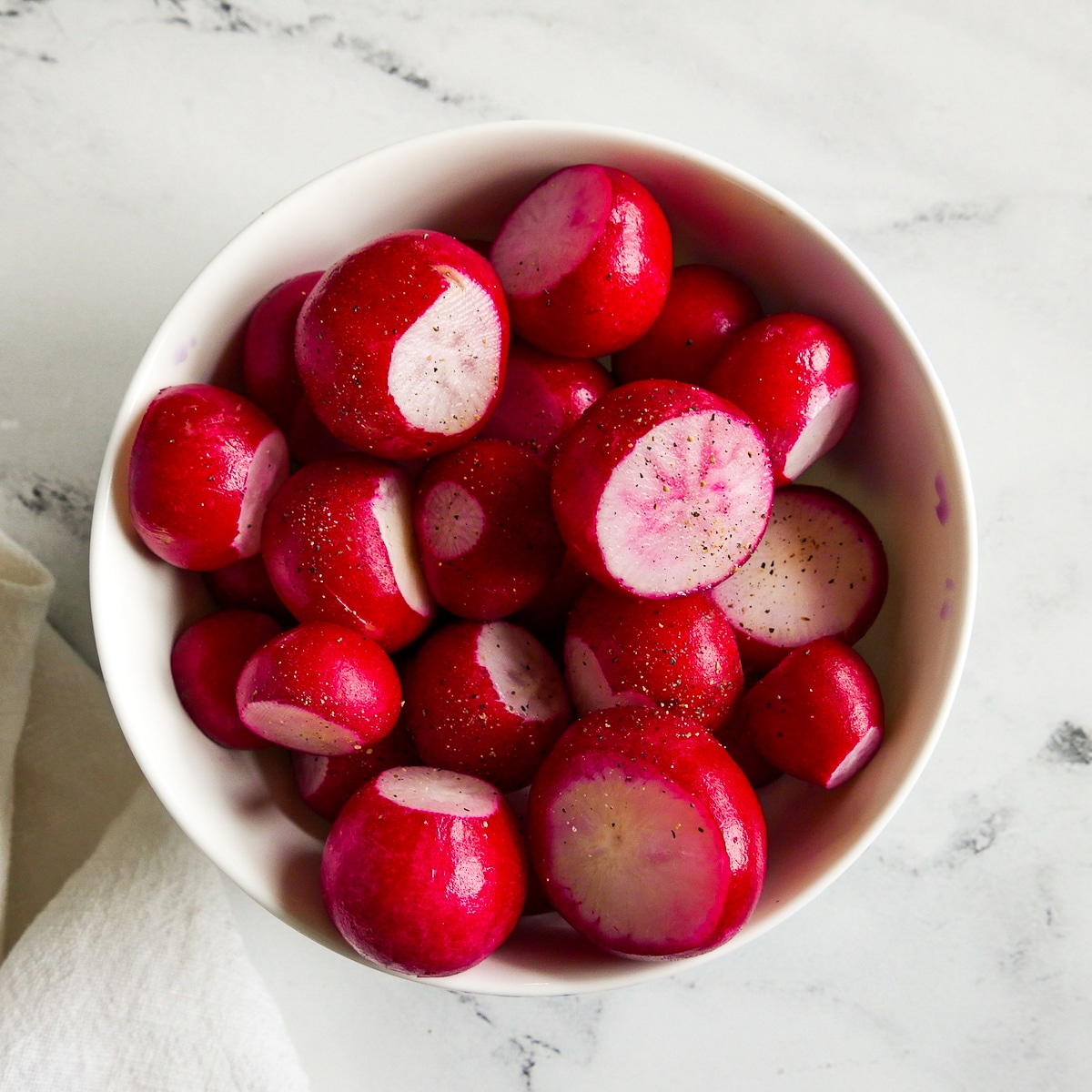 trimmed radishes tossed with olive oil in a white bowl.