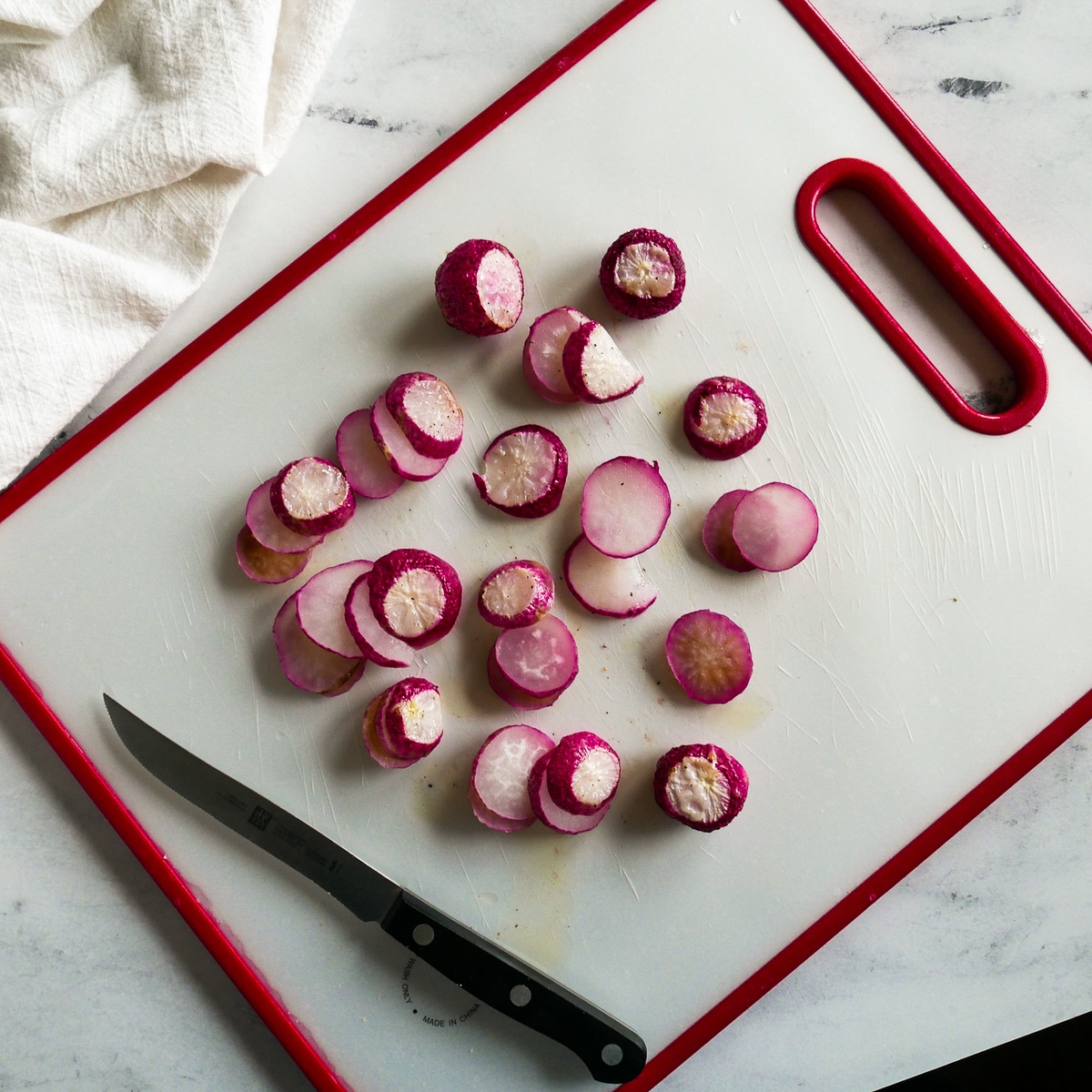 sliced radishes on a white cutting board with a knife.