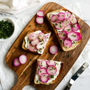 Roasted radish toast arranged on a cutting board with fresh chives.