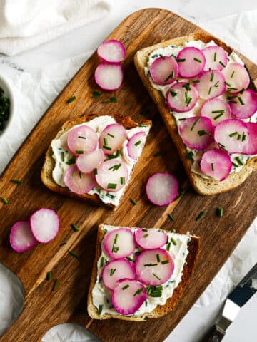 Roasted radish toast arranged on a cutting board with fresh chives.