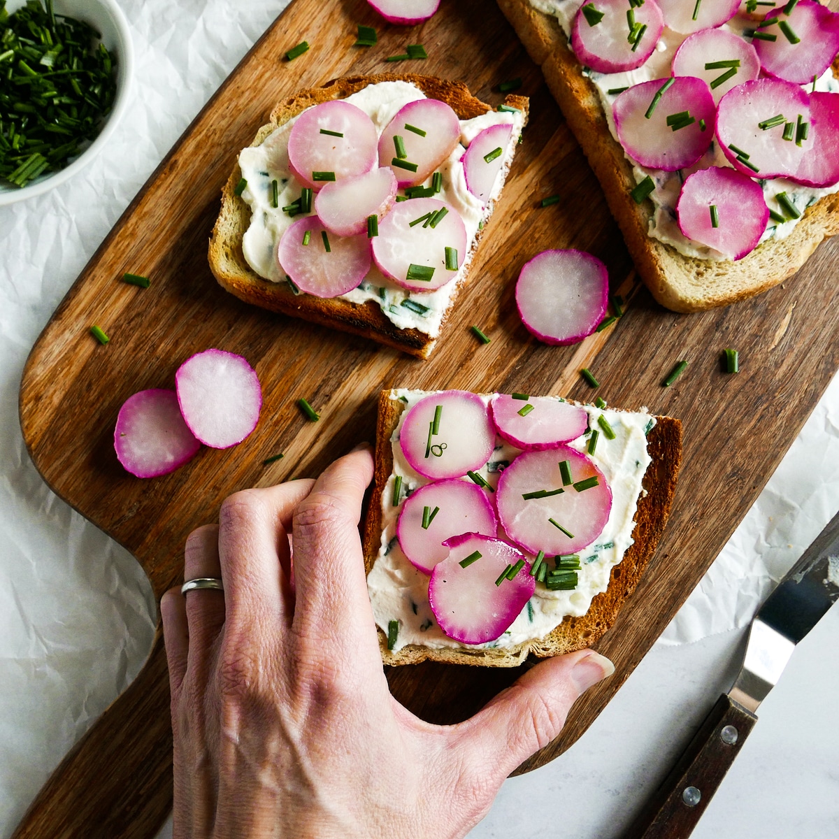 white hand picking up a piece of toasts with ricotta.