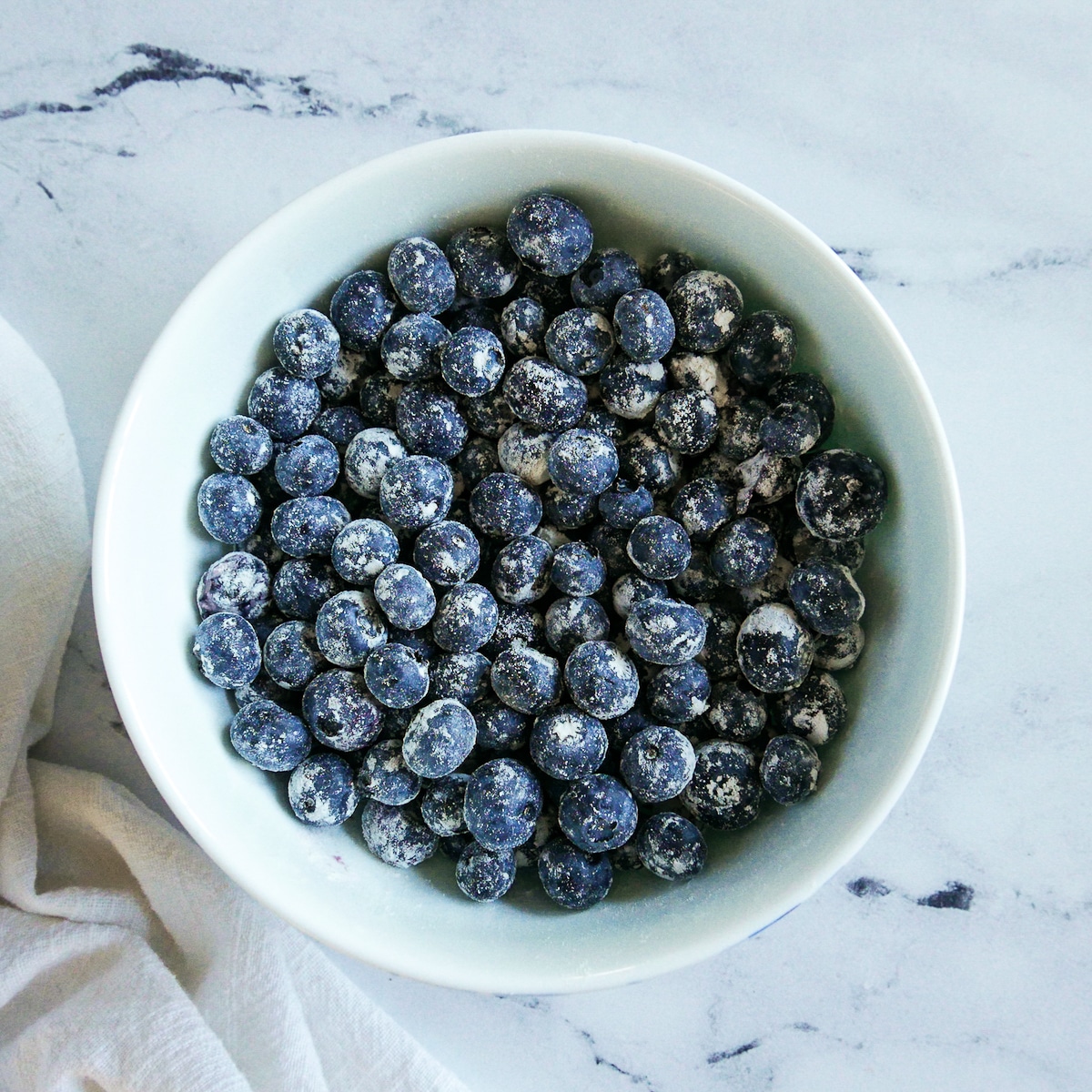 Blueberries tossed with flour in a white bowl.