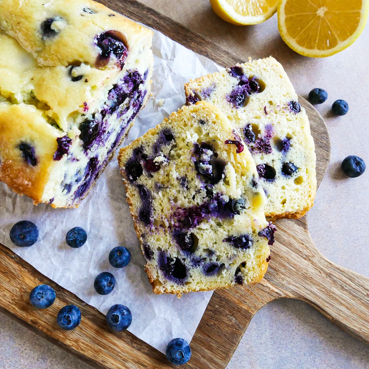 lemon pound cake sliced onto parchment paper with fresh blueberries.