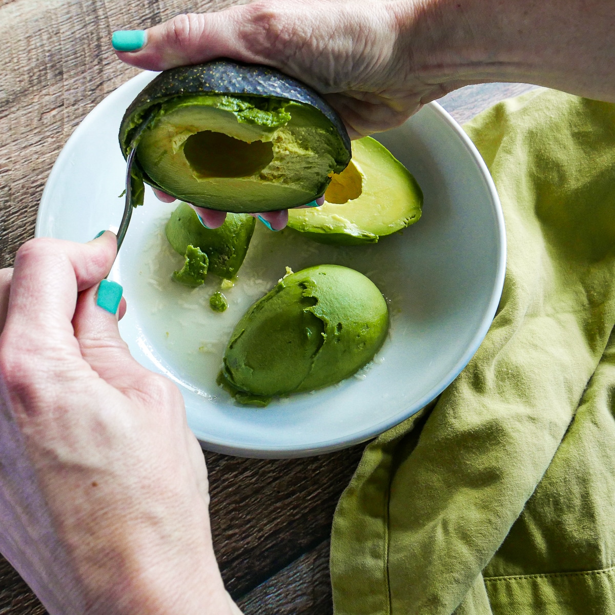 Hand scooping out a pitted avocado into a bowl.