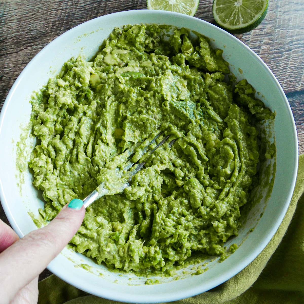 Fork mashing avocado in a white bowl.