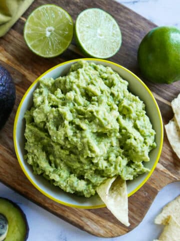 cup of simple guacamole with chips and lime on the side.