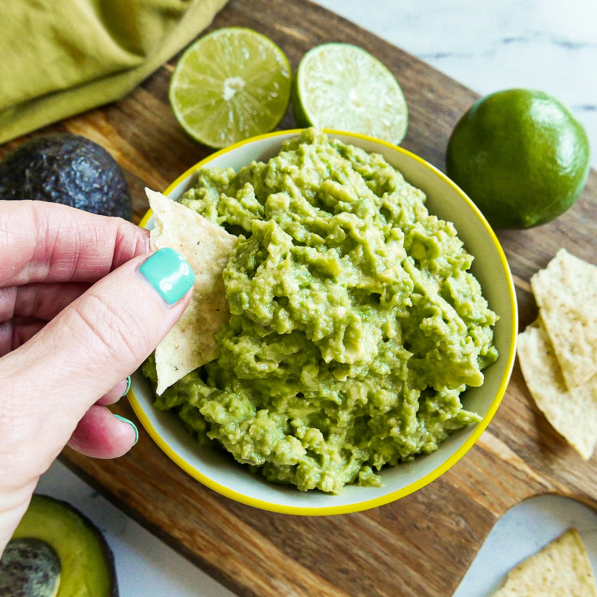 hand dipping tortilla chip into 4 ingredient guacamole.