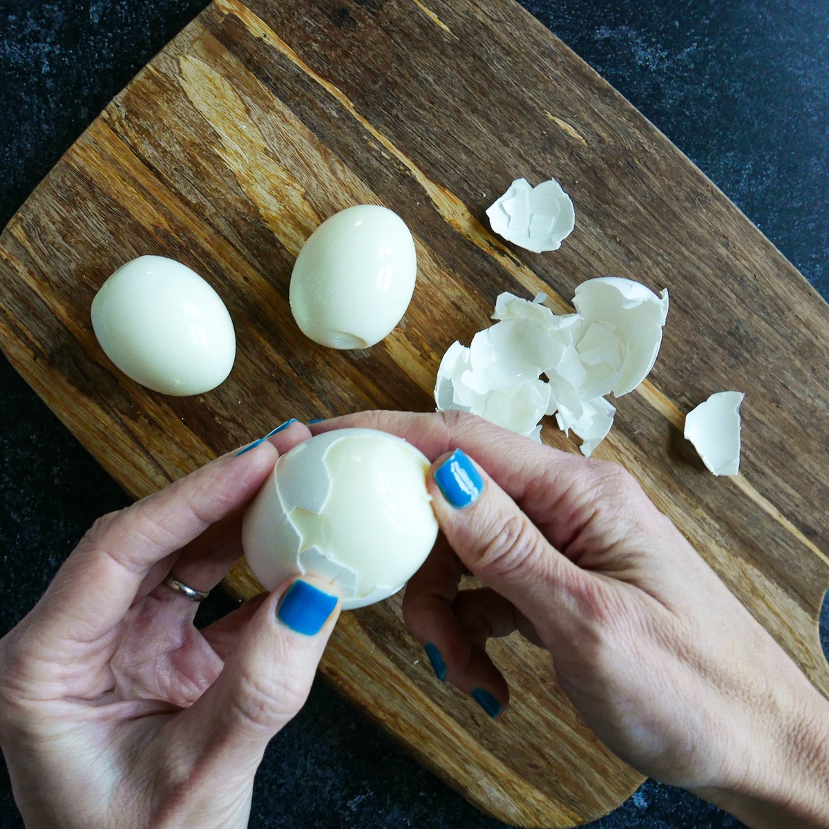 white hand peeling hard boiled eggs.