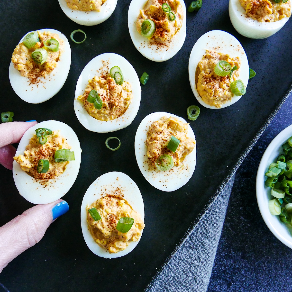 hand-picking-up-egg.jpg hand picking up a sriracha deviled egg from a platter.