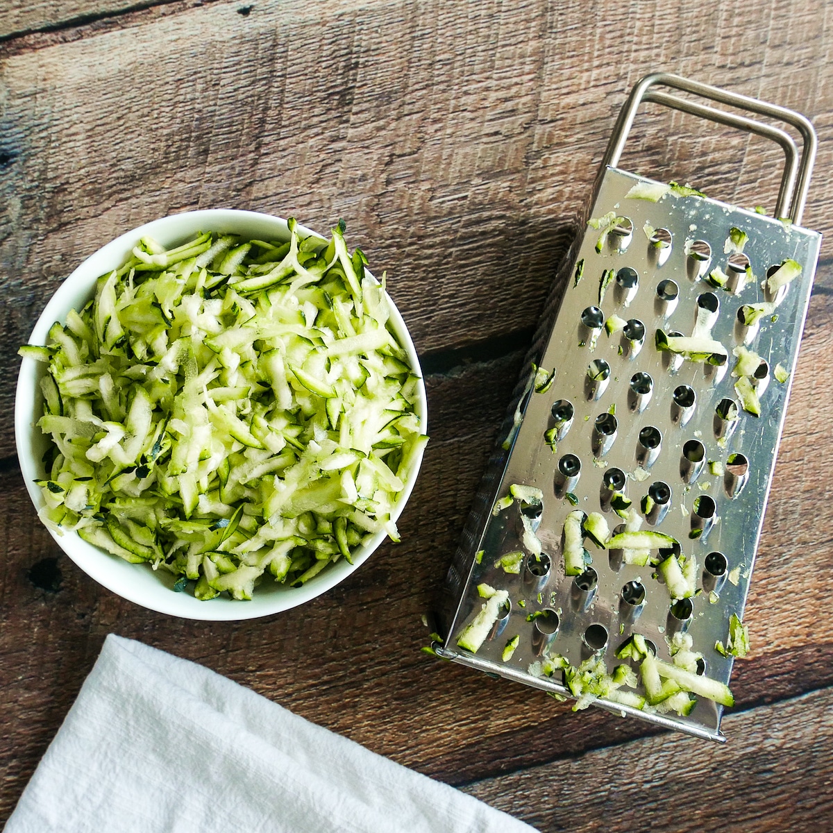 Box grater resting next to a bowl full of grated zucchini.