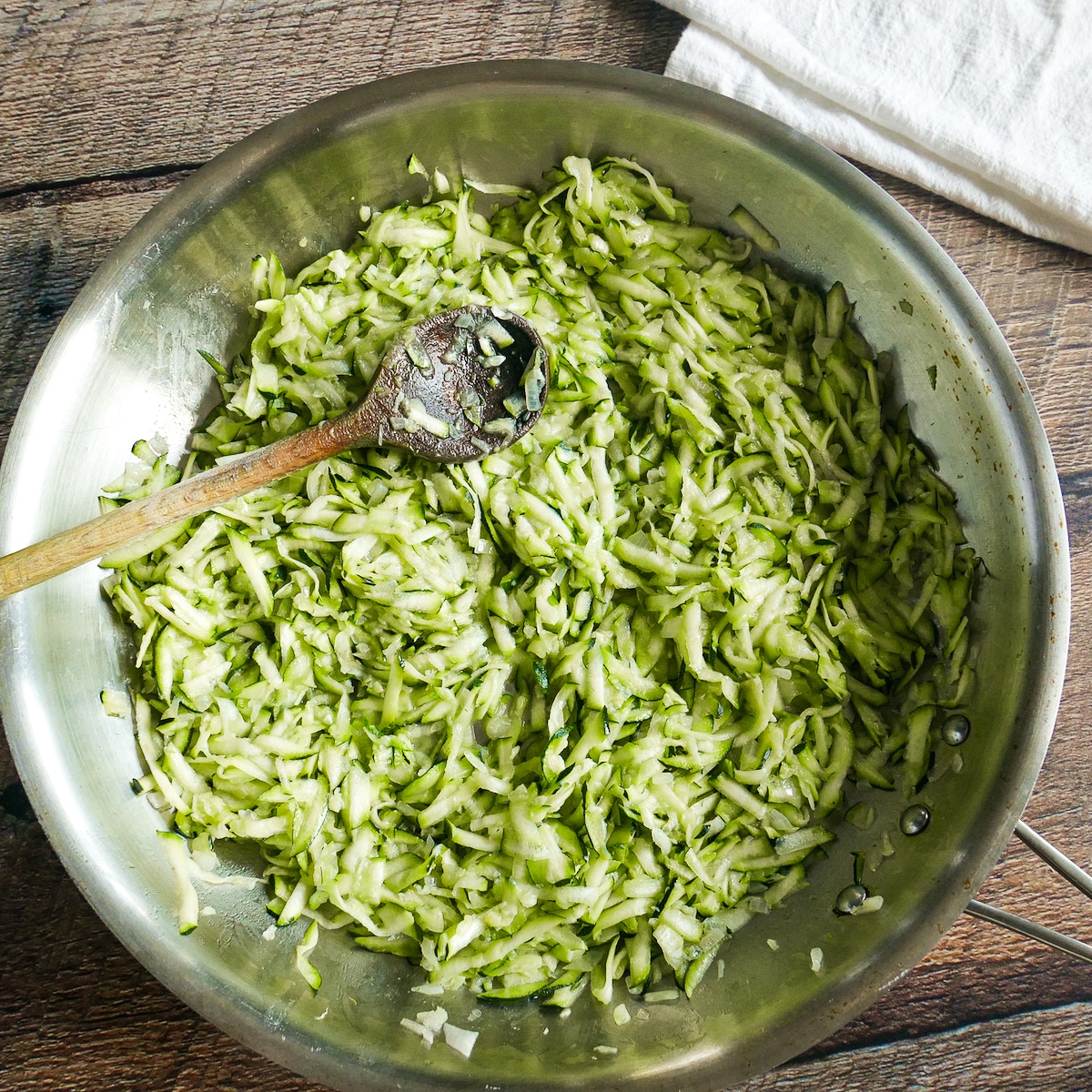 Shredded zucchini added to skillet with shallots and garlic.