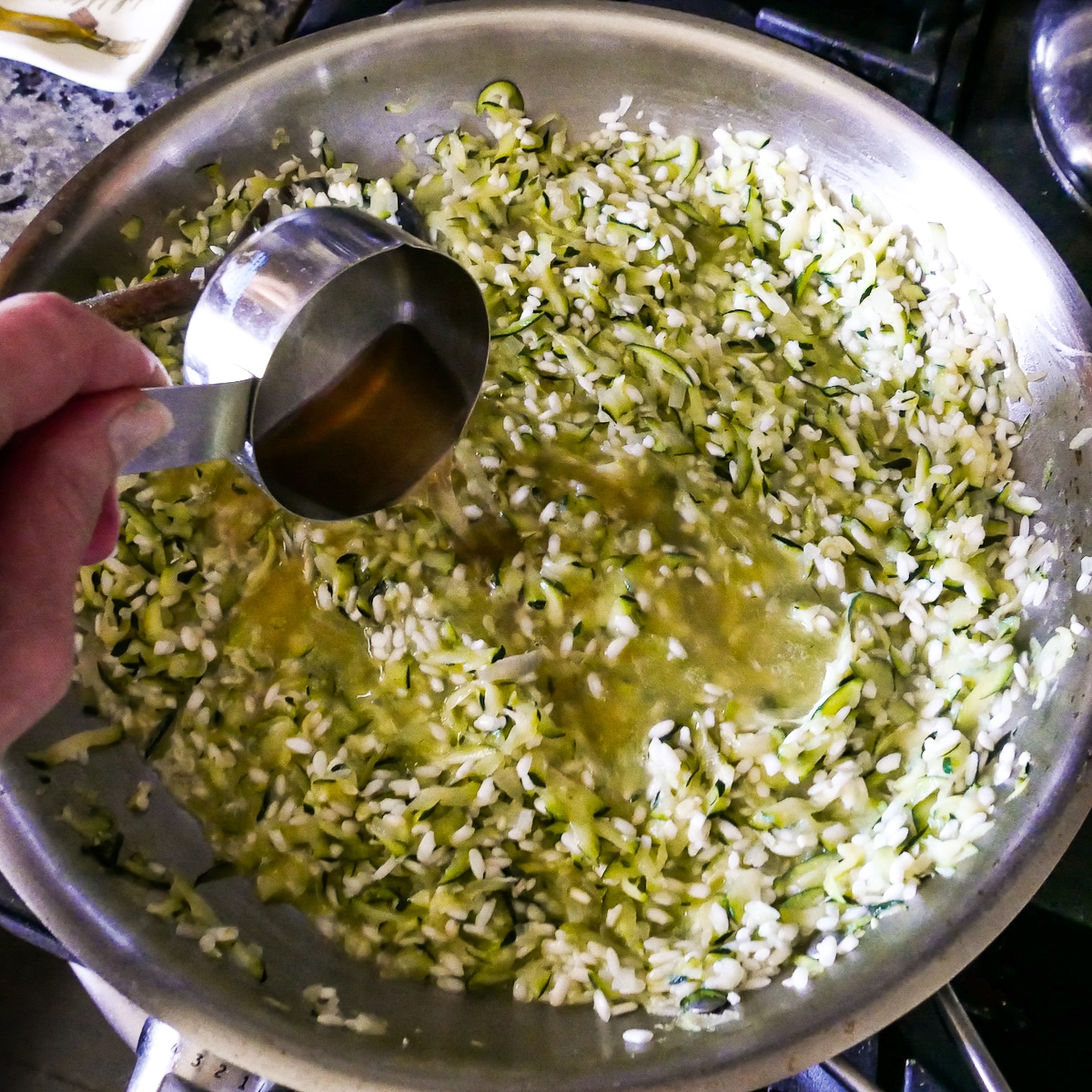 Warmed vegetable broth being added to rice and zucchini mixture.