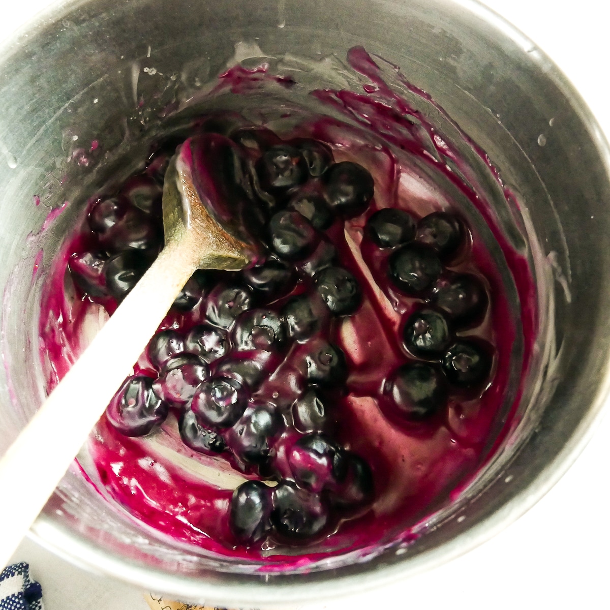 Thickened blueberry filling in a saucepan with a wooden spoon.