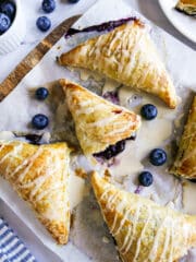 Blueberry turnovers arranged on parchment paper with one torn open.