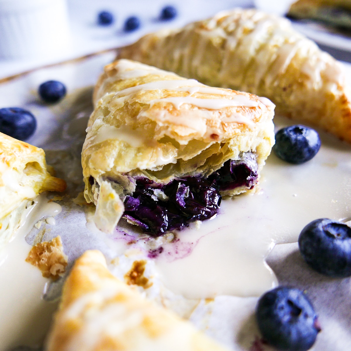 Puff pastry blueberry turnover cut in half with fresh blueberries next to it.