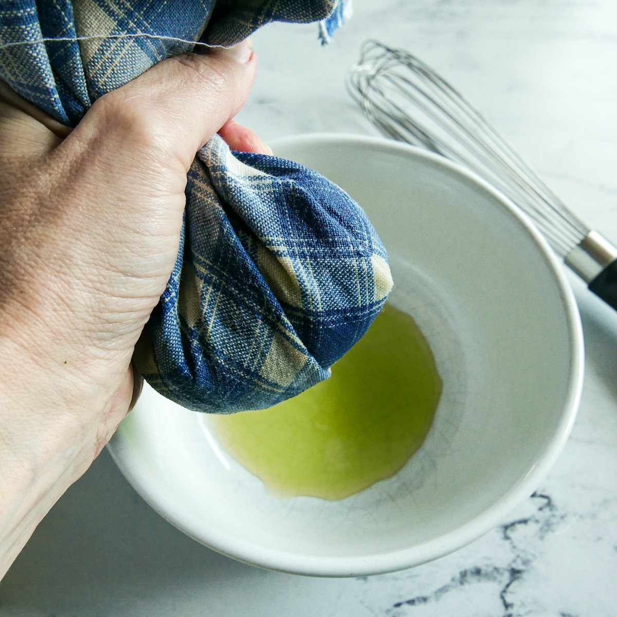 Hand squeezing water out of shredded zucchini into a bowl.