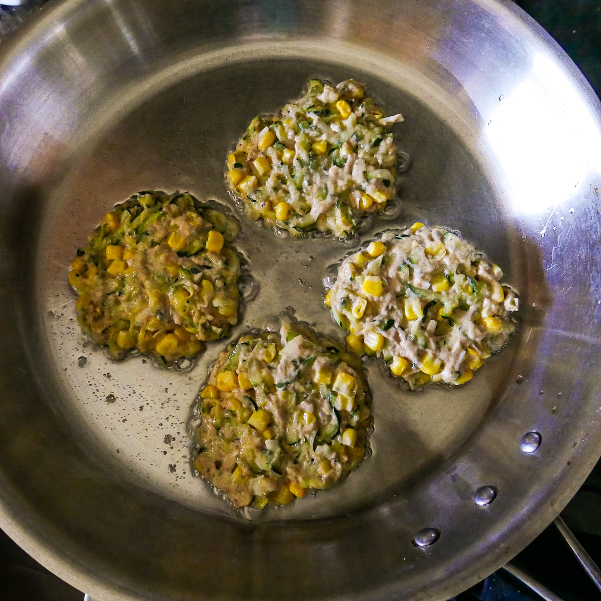 Fritters cooking in a large skillet.