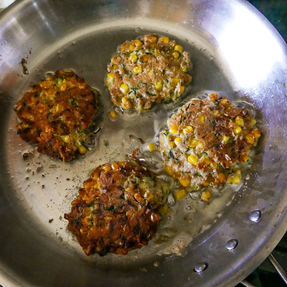 Golden brown fritters frying in skillet after being flipped.