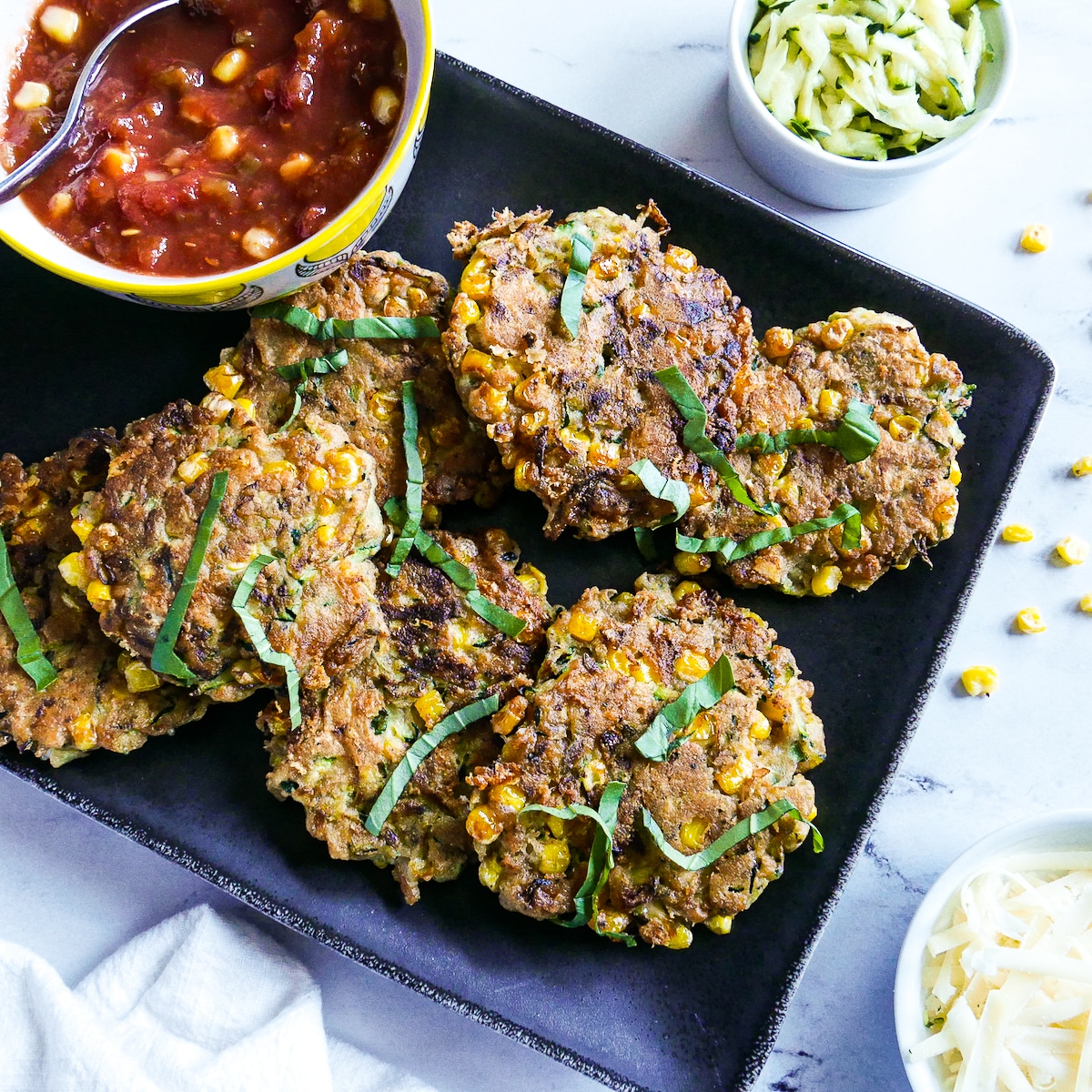 Zucchini fritters with corn arranged on a black platter with salsa.