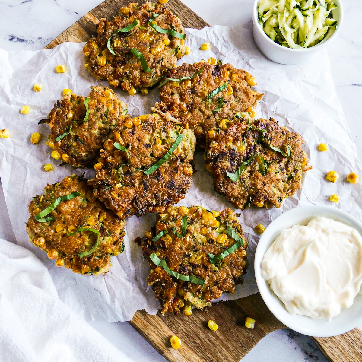 Zucchini and corn fritters arranged on parchment paper with a cup of sauce.