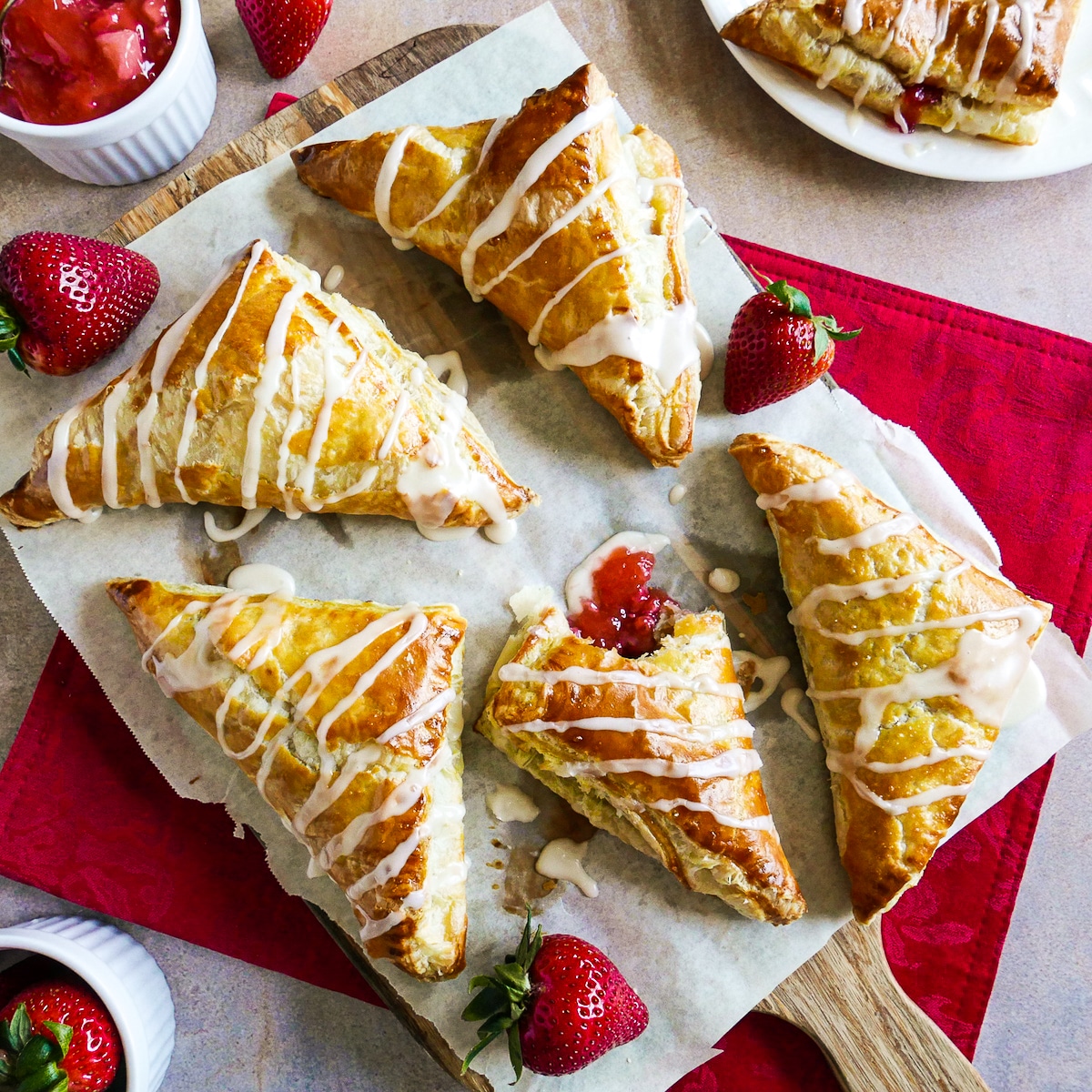 Strawberry turnovers arranged on parchment paper with fresh strawberries.