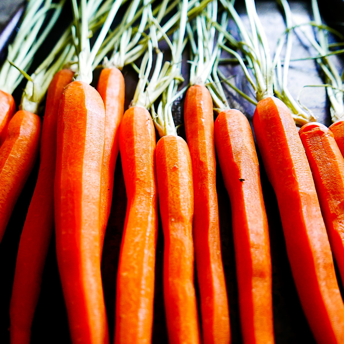 Peeled carrots arranged on a baking sheet.