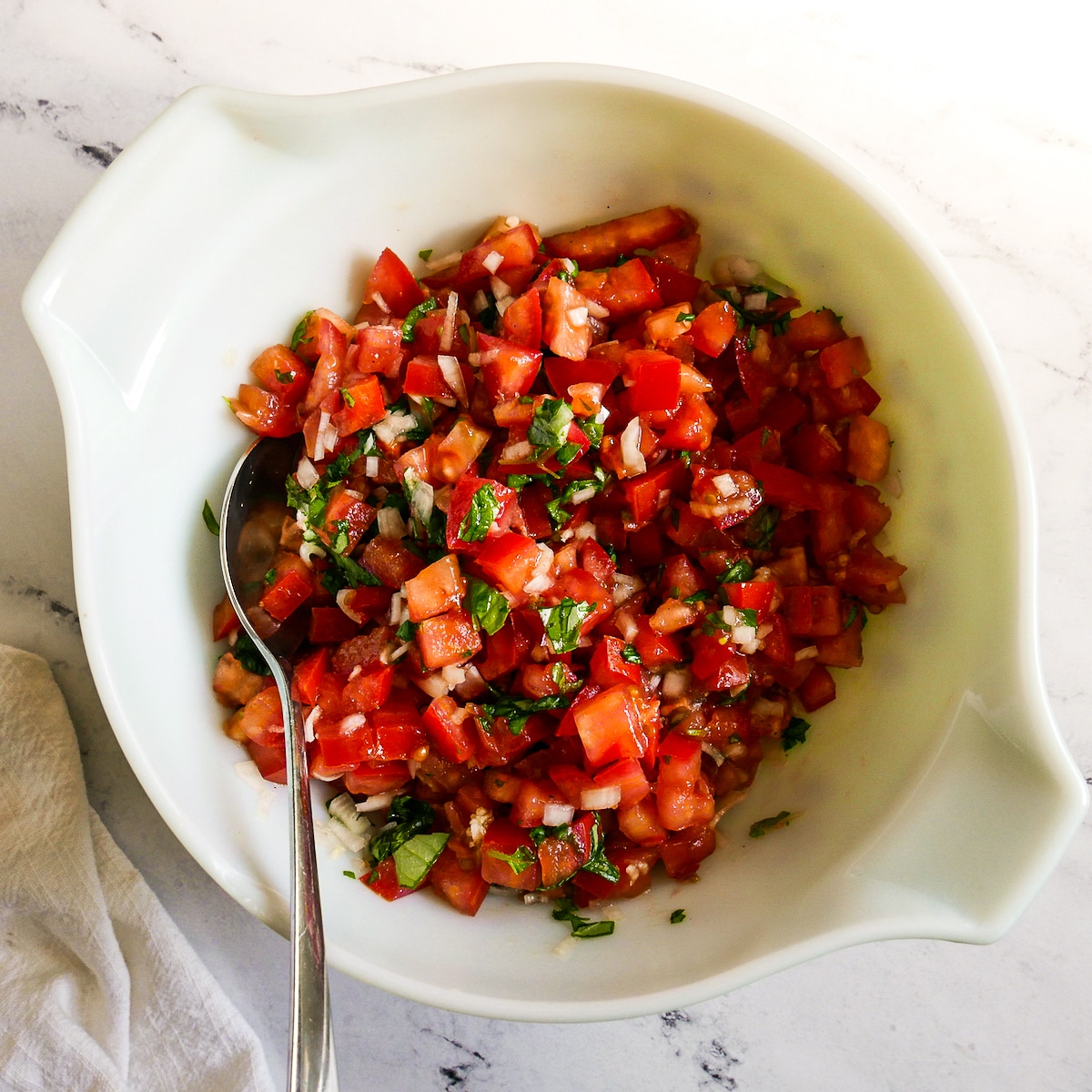 Tomato mixture combined in a medium bowl with a spoon.