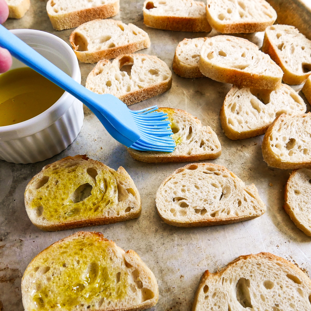 Brushing olive oil onto a sliced baguette.