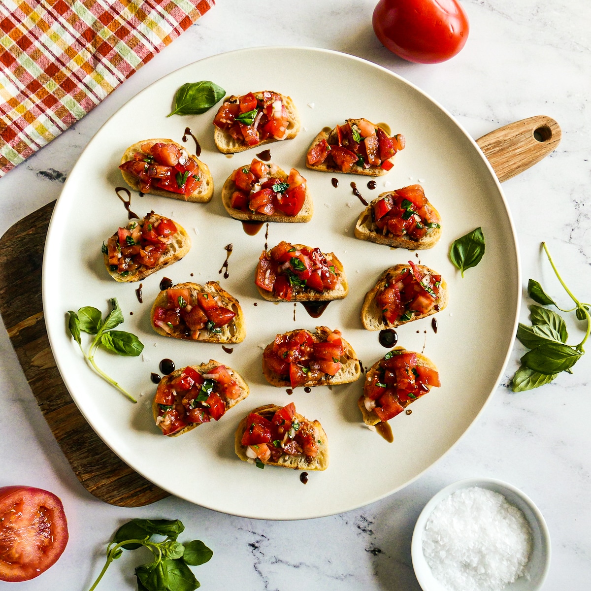 Bruschetta drizzled with balsamic glaze arranged on a white platter.