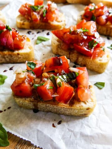 Balsamic bruschetta arranged on parchment paper with fresh basil.