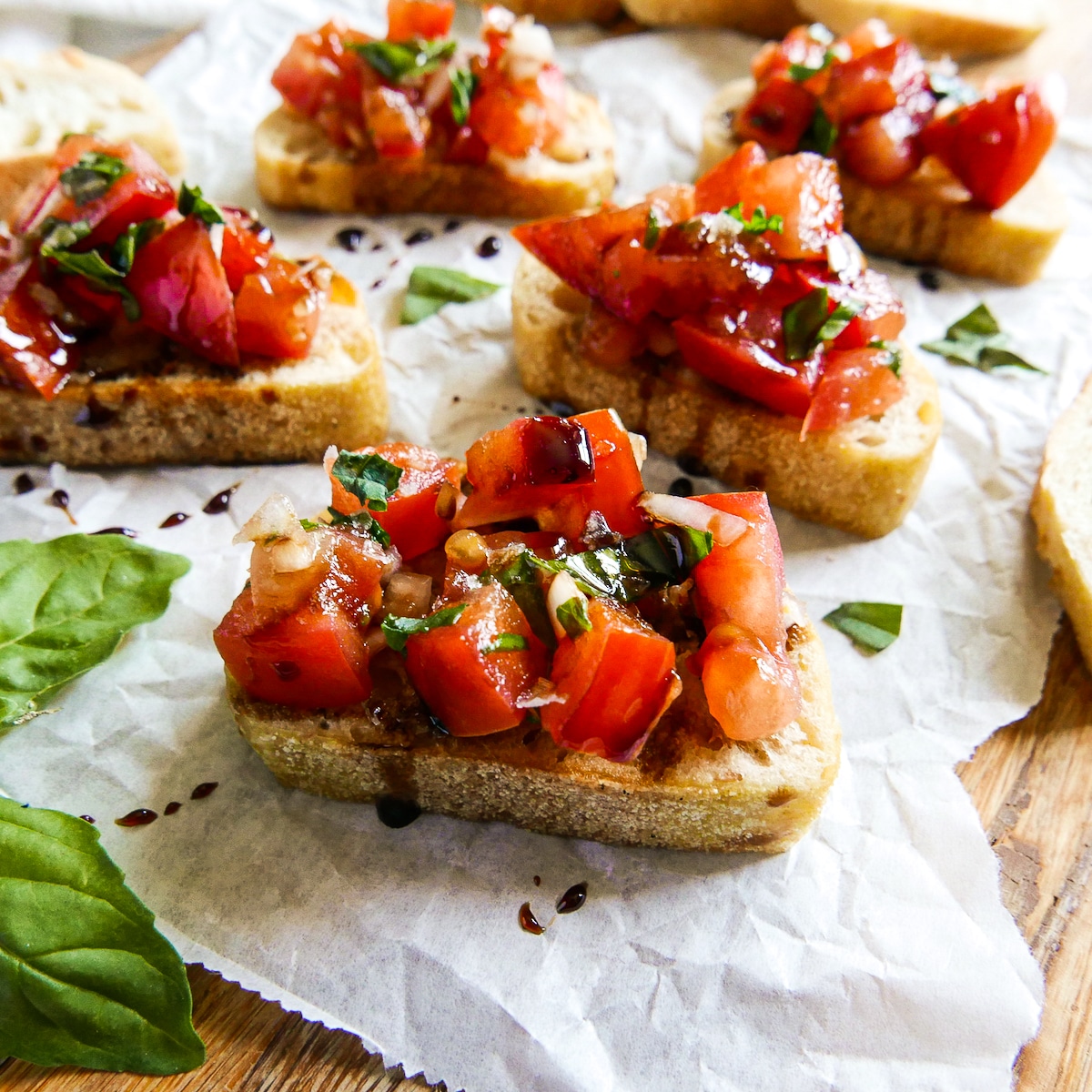 Balsamic bruschetta arranged on parchment paper with fresh basil.