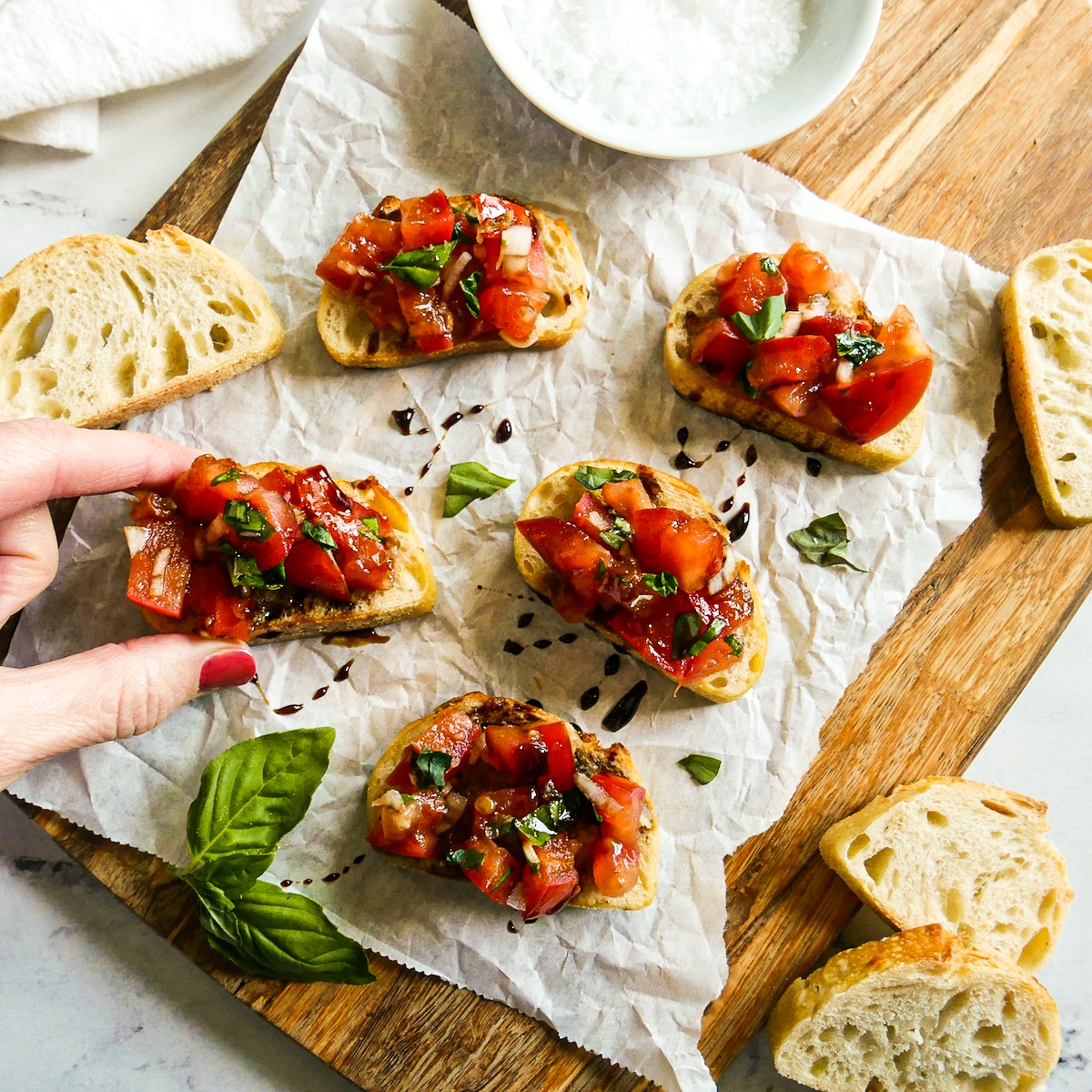 Hand picking up a bruschetta appetizer from a cutting board.