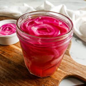 Jar of quick pickled onions resting on a cutting board.