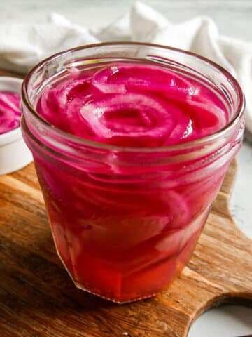 Jar of quick pickled onions resting on a cutting board.