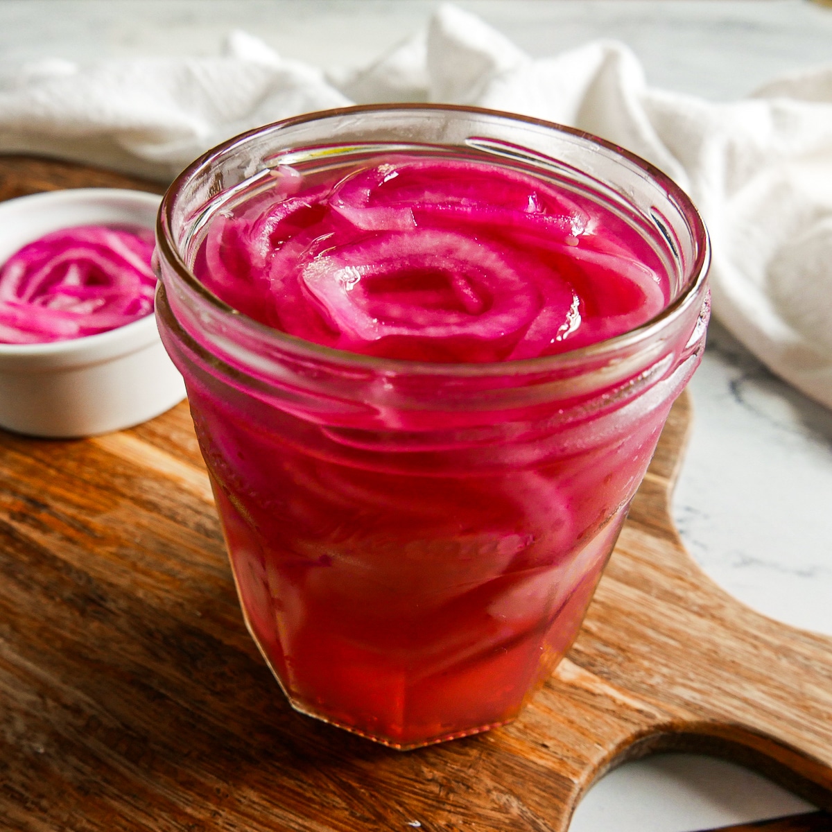 Jar of quick pickled onions resting on a cutting board.