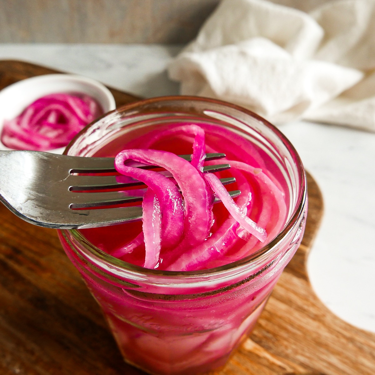 Fork lifting up pickled onions from a jar.