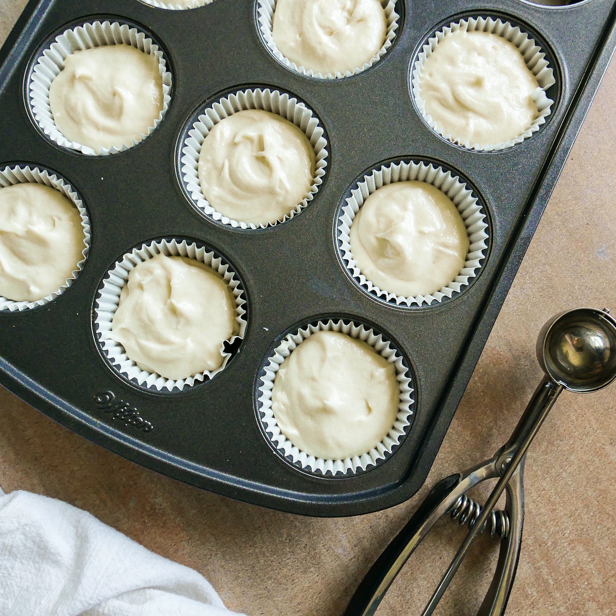 Cupcake batter scooped into lined muffin tin.