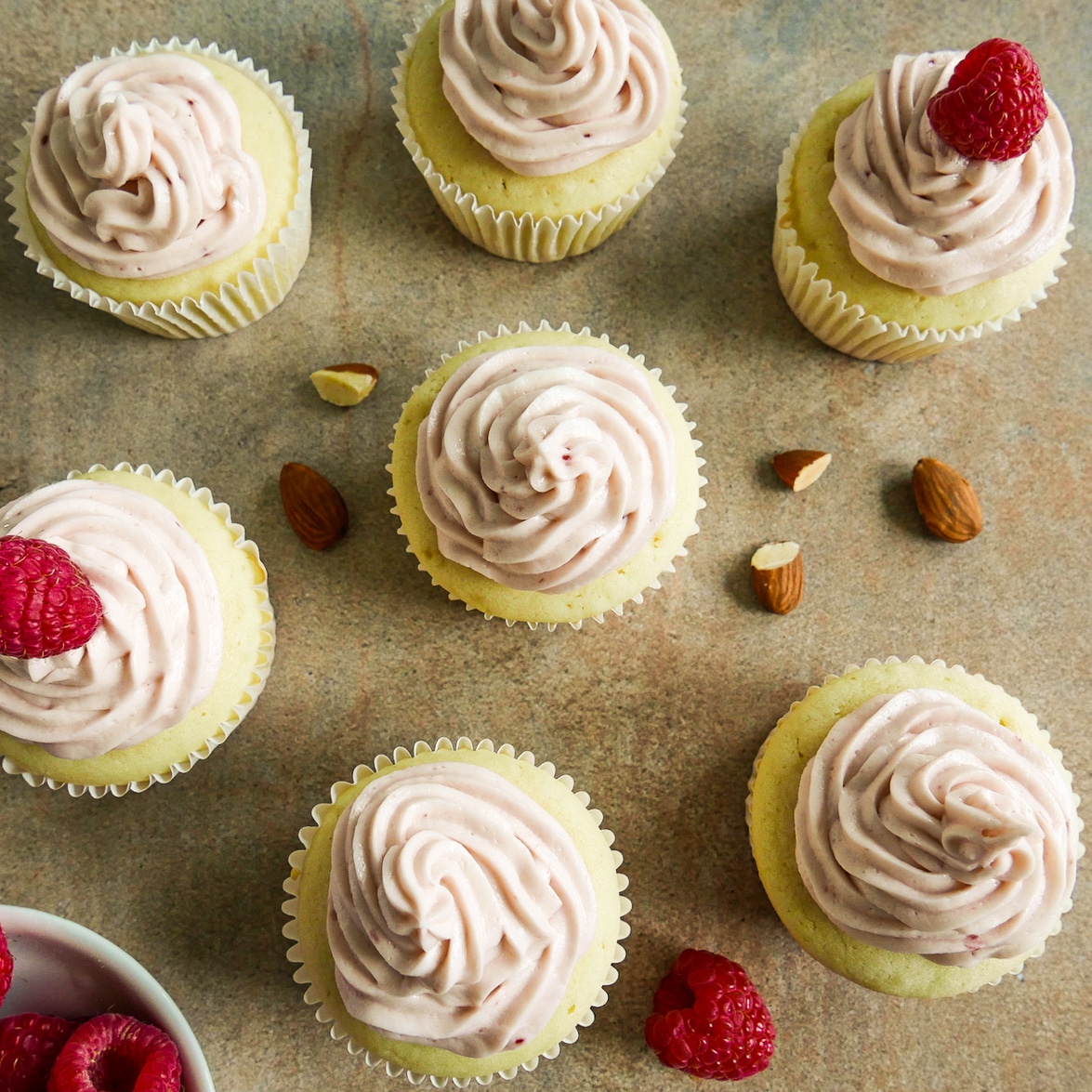 Cupcakes garnished with fresh raspberries arranged on a table.