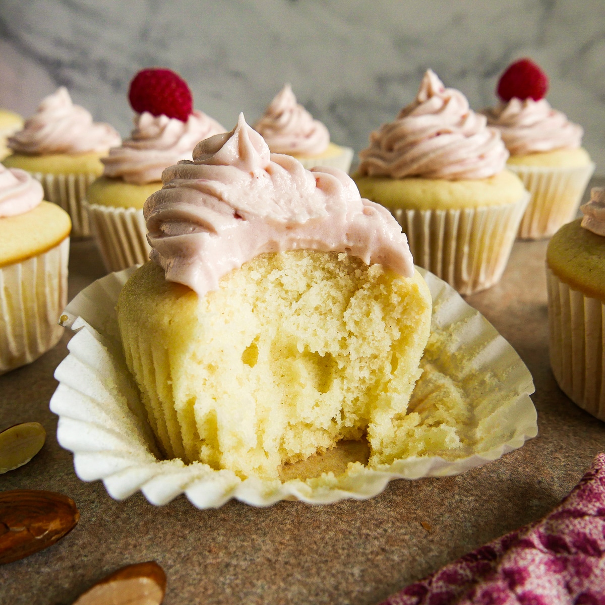 Frosted cupcake with a bite taken out of it resting on a table.