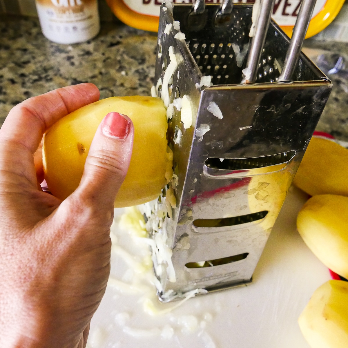 Hand shredding a potato on a box grater.