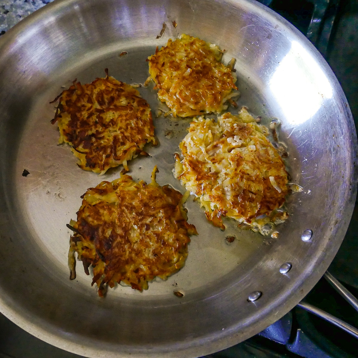 Golden and crispy fritters after being flipped in a frying pan.