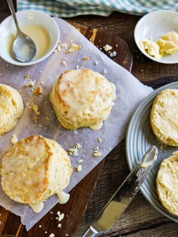 Buttermilk biscuits on a plate and cutting board with cup of maple cream and spoon.