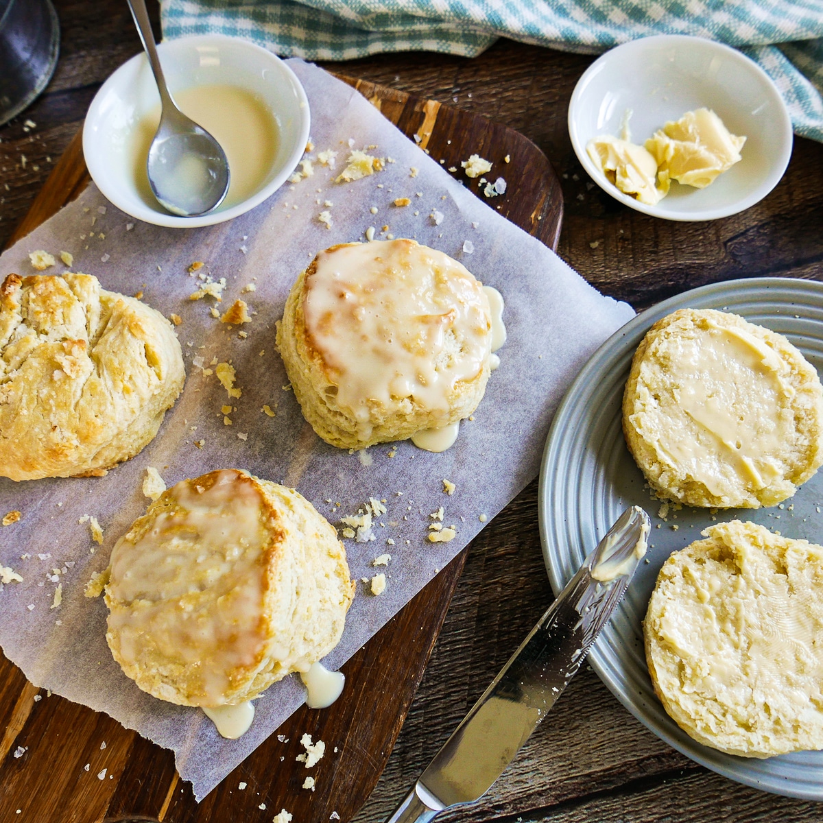 Buttermilk biscuits on a plate and cutting board with cup of maple cream and spoon.