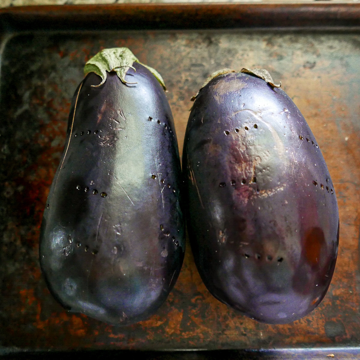 two pierced eggplants on a baking sheet.