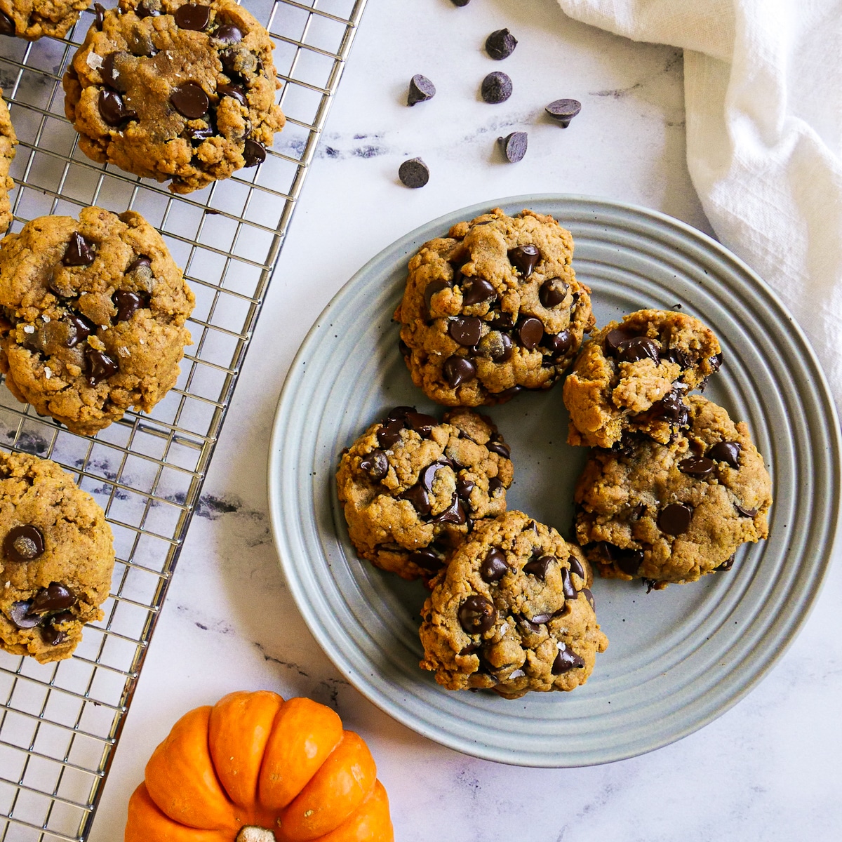 Chocolate chip cookies arranged on a plate and cooling rack with a mini pumpkin. 